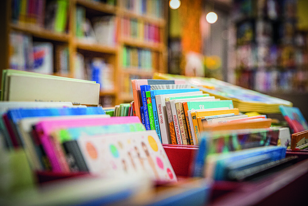 Nahaufnahme von bunten Büchern, die aufrecht in den Regalen einer Buchhandlung stehen; im Hintergrund sind weitere Bücher und verschwommene Regale zu sehen.