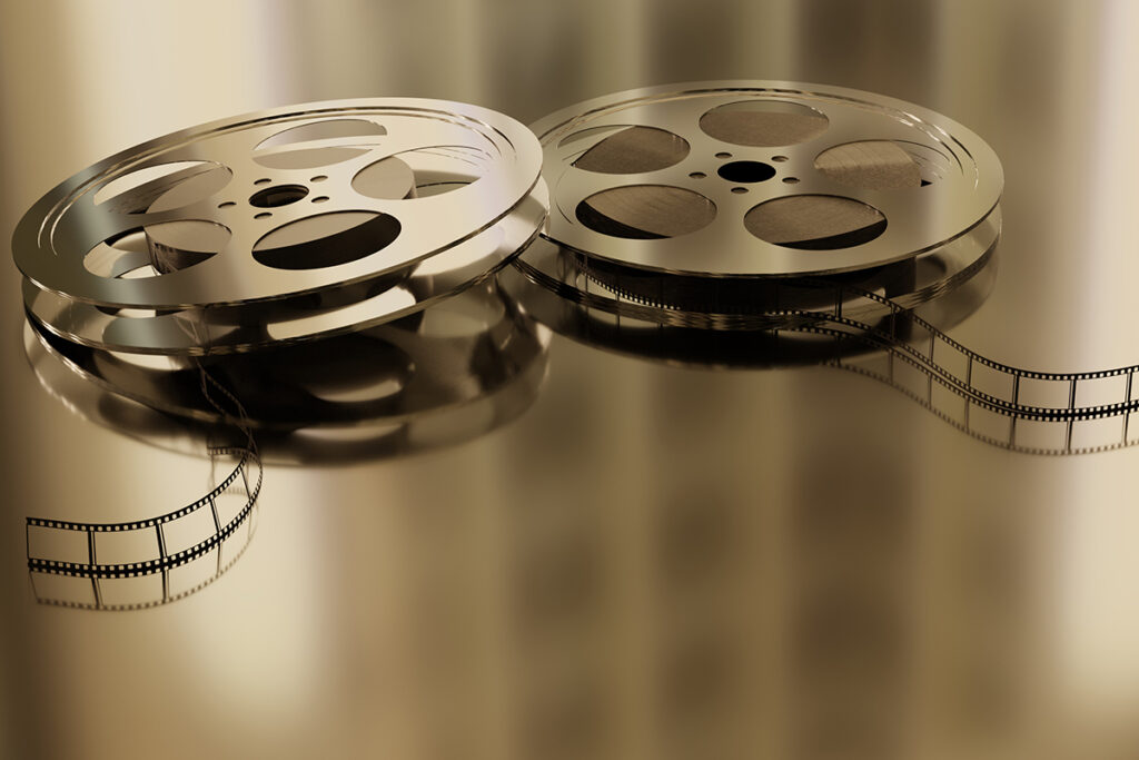 Zwei Filmspulen aus Metall, aus denen Filmstreifen abgewickelt sind und die auf einer spiegelnden goldenen Oberfläche liegen.