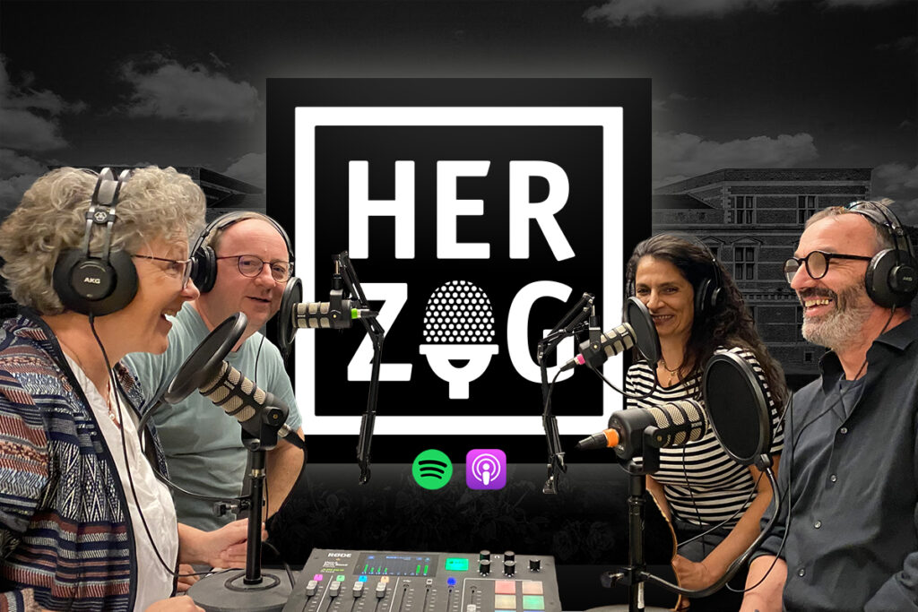 Vier Personen mit Kopfhörern sitzen um Mikrofone herum und nehmen einen Podcast auf; hinter ihnen ist das HERZOG-Podcast-Logo zu sehen, und auf dem Tisch steht die Tonausrüstung.