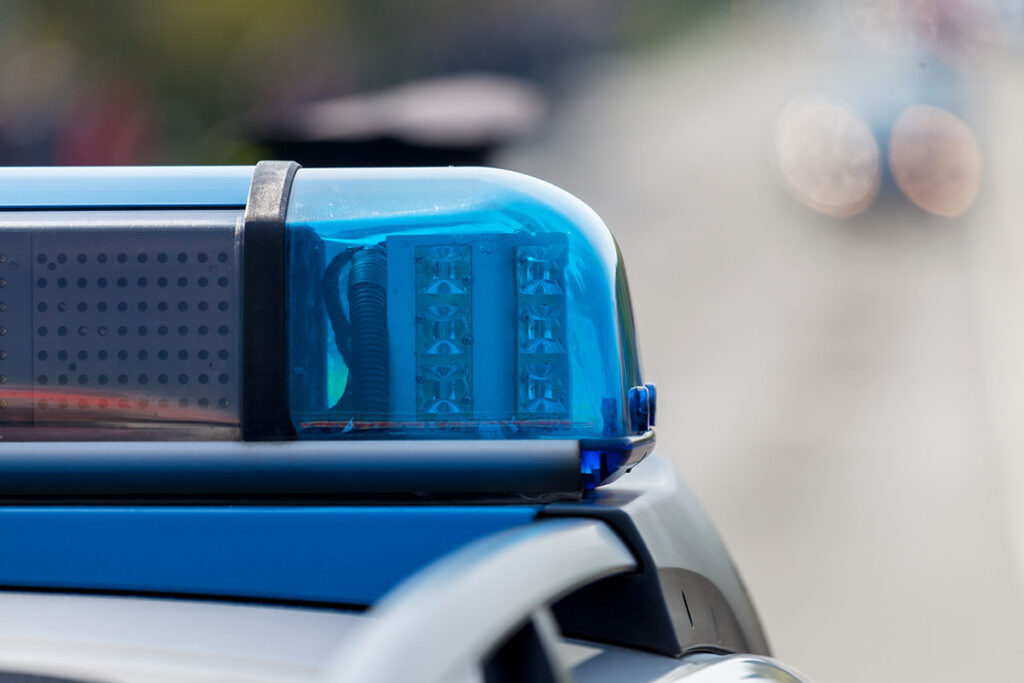 Nahaufnahme einer blauen Polizeisirene mit einer verschwommenen Straße und Fahrzeugen im Hintergrund.