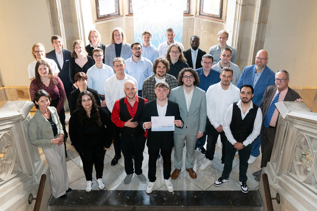 Eine große Gruppe von Menschen posiert auf einer Treppe für ein Foto; in der Mitte steht eine Person, die eine Urkunde mit der Aufschrift Kreis Düren in der Hand hält.