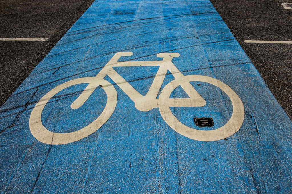 Ein weißes Fahrradsymbol, das auf einen blauen Asphaltstreifen gemalt ist, der einen Fahrradstreifen markiert.