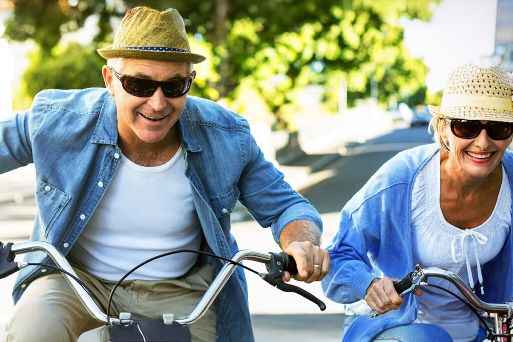 Ein Mann und eine Frau, die Sonnenbrillen und Hüte tragen und draußen Fahrrad fahren.