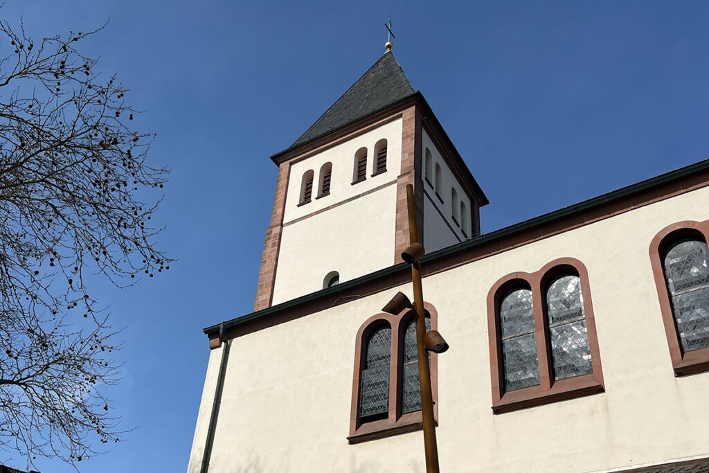 Eine Kirche mit weißer Fassade, Bogenfenstern und einem quadratischen Glockenturm vor strahlend blauem Himmel.