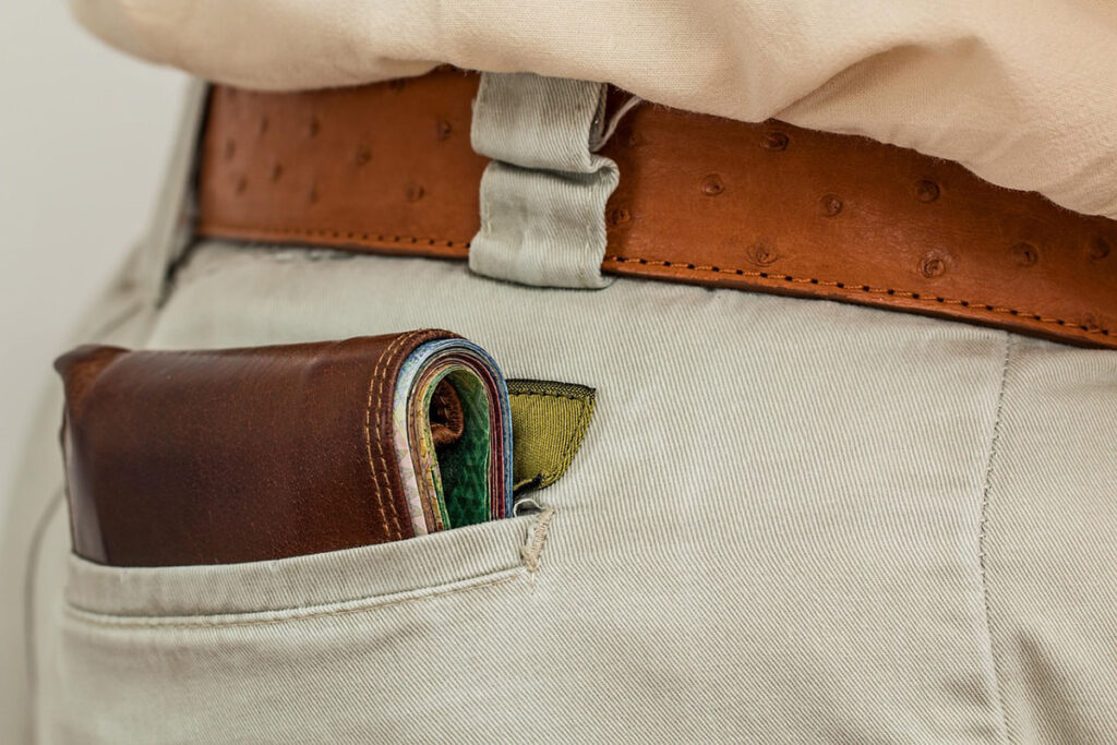 Eine braune Lederbrieftasche, die in der Gesäßtasche einer hellen Hose steckt, die mit einem hellbraunen Gürtel befestigt ist.