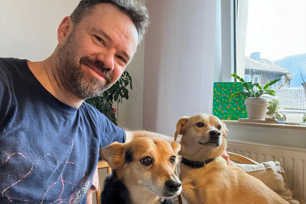 Ein Mann, der lächelt, während er neben zwei Hunden sitzt.